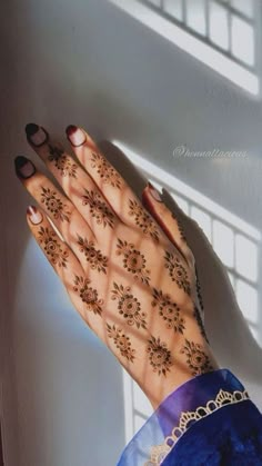 a woman's hands with henna tattoos on her arm and hand, in front of a window