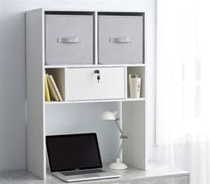 a laptop computer sitting on top of a desk next to a white book shelf with bins