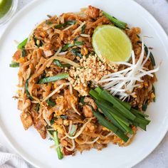 a white plate topped with pad thai noodles and green onions next to a lime wedge