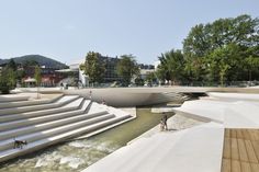 people are walking around in the open area next to a river with steps leading up to it