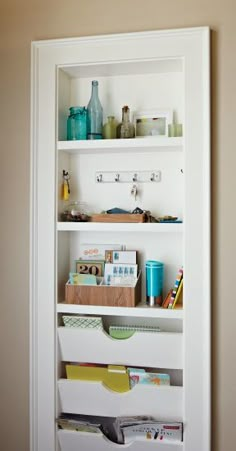 a white book shelf filled with lots of books and other items next to a wall