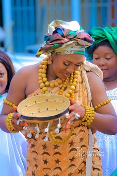 a woman holding a bowl with beads around her neck and wearing a headdress