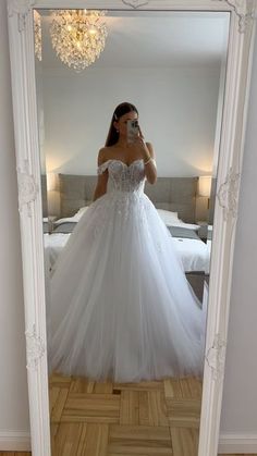 a woman taking a selfie in front of a mirror wearing a white wedding dress