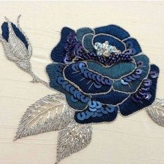 a close up of a blue flower on a white cloth with silver leaves and beads