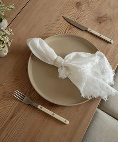 a plate with a piece of cloth on it next to a knife, fork and flower vase