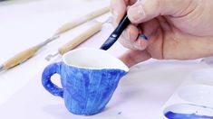 a person is painting a blue cup on a table