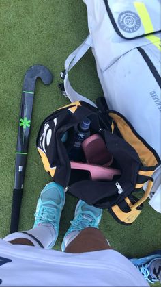 a person standing next to a backpack and golf club on the grass with their feet propped up