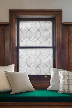 a window seat with several pillows on it in front of a wooden frame and wall