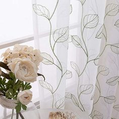 a vase filled with flowers sitting next to a window covered in sheers and curtains