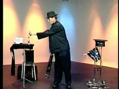 a man in a black suit and top hat standing next to a table with two stools