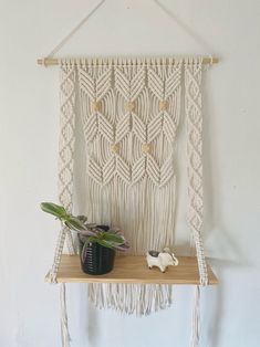 a macrame wall hanging next to a potted plant on a wooden shelf