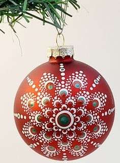 a red ornament hanging from a tree branch with white and green designs on it