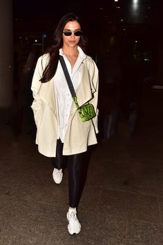 a woman in white shirt and black leggings carrying a green purse while walking through an airport