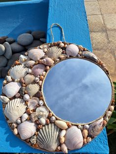 a mirror sitting on top of a blue bench next to rocks and pebbles in the grass