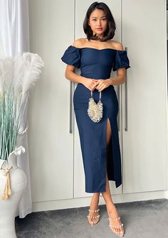 a woman standing in front of a white cabinet wearing a navy blue dress with an off the shoulder design