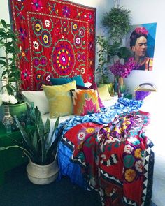 a bed covered in colorful blankets and pillows next to a potted plant on the floor