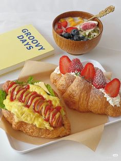 two croissants with strawberries on them are next to a bowl of fruit