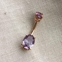 an amethyst purple stone sits on top of a gold barbell earring