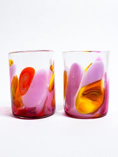 two colorful glass cups sitting next to each other on a white surface with no one around them