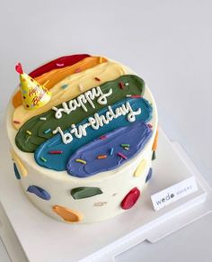 a birthday cake with the words happy birthday written on it and colorful icing, sitting on top of a white surface