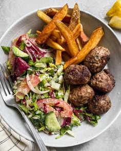 a white plate topped with meatballs, salad and french fries