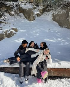 four women sitting on a log in the snow together, with one woman holding another