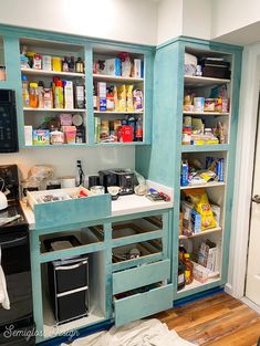 a kitchen with blue cabinets and shelves filled with food, drinks and other items in it