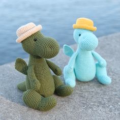 two crocheted stuffed animals sitting next to each other on the ground near water