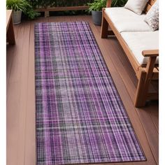 a purple and black rug on a wooden deck next to a bench with plants in the background