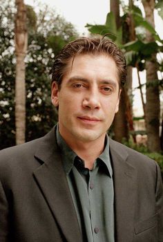 a man in a suit and green shirt posing for a photo with trees in the background