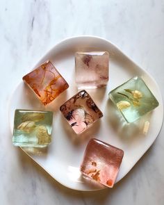 five different colored glass cubes on a white plate with marble counter top in the background