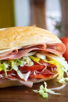 a sub sandwich with meat, lettuce and tomatoes on a wooden cutting board