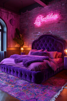 a bed with purple sheets and pillows in front of a brick wall that has a neon sign above it