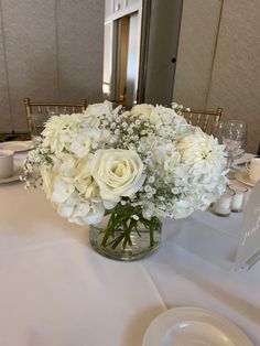 a vase filled with white flowers sitting on top of a table next to a plate