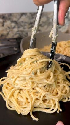 someone using tongs to stir noodles in a pan