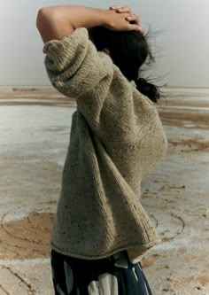 a woman standing in the desert with her back to the camera and arms behind her head