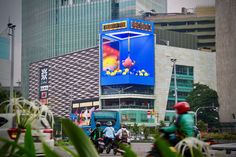 two people on motorbikes driving down the street in front of a large billboard