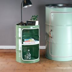 a green metal trash can sitting next to a lamp on top of a wooden floor