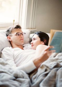 a man and woman laying in bed reading a book