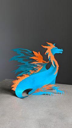 a blue and orange dragon sculpture sitting on top of a cement floor next to a gray wall