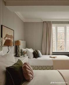 two beds in a hotel room with striped walls and curtains on the windowsills