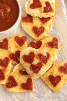 small heart shaped pizzas on top of wax paper with sauce in the bowl next to them