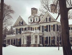 a large white house with black shutters on the front and side windows in winter