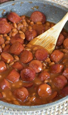 beans and sausage are being cooked in a pan with a wooden spoon on the side