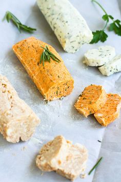 some crackers and cheese are on a piece of wax paper with herbs sprinkled on them