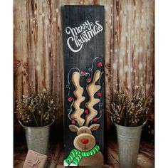 a wooden sign that says merry christmas with a reindeer and candy cane in front of some potted plants