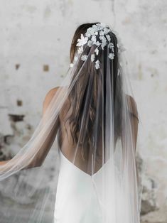 the back of a bride's veil with flowers and leaves on it, in front of a brick wall