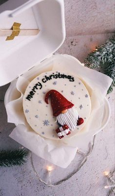 a decorated christmas cookie with a santa hat on it sitting in a white box next to some lights