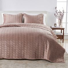 a bed with pink comforter and pillows in a room next to a white wall