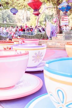 many colorful cups and saucers are on display at the amusement park with people in the background